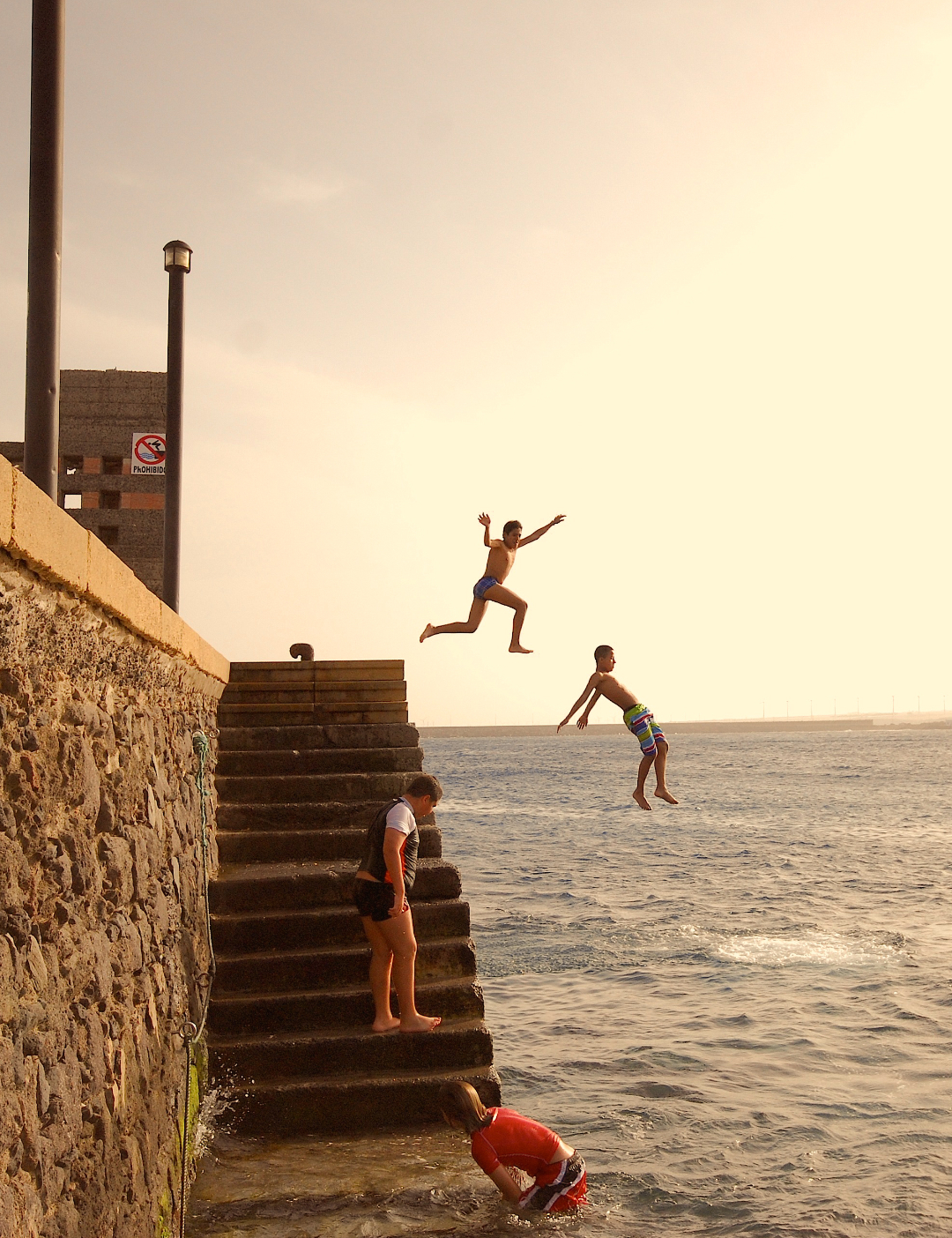 Personas saltando al mar desde el muelle de Playa de Arinaga al atardecer, en Gran Canaria